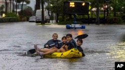 Matthew Koziol, Matías Ricci, Manuel Ricci y Raúl Fernández viajan en balsa por una calle inundada por las fuertes lluvias en North Bay Road en Sunny Isles Beach, Florida, el miércoles 12 de junio de 2024