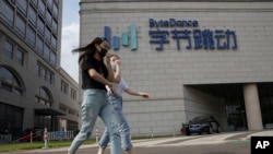 ARCHIVO - En esta fotografía de archivo del 7 de agosto de 2020, mujeres que usan máscaras para evitar la propagación del coronavirus conversan mientras pasan por la sede de ByteDance, propietarios de TikTok, en Beijing, China.