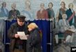 La gente examina una papeleta en un colegio electoral ubicado en una escuela durante las elecciones presidenciales en San Petersburgo, Rusia, el sábado 16 de marzo de 2024, con una pintura que representa a la zarina rusa Catalina II y sus contemporáneos en la pared.