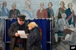 La gente examina una papeleta en un colegio electoral ubicado en una escuela durante las elecciones presidenciales en San Petersburgo, Rusia, el sábado 16 de marzo de 2024, con una pintura que representa a la zarina rusa Catalina II y sus contemporáneos en la pared.